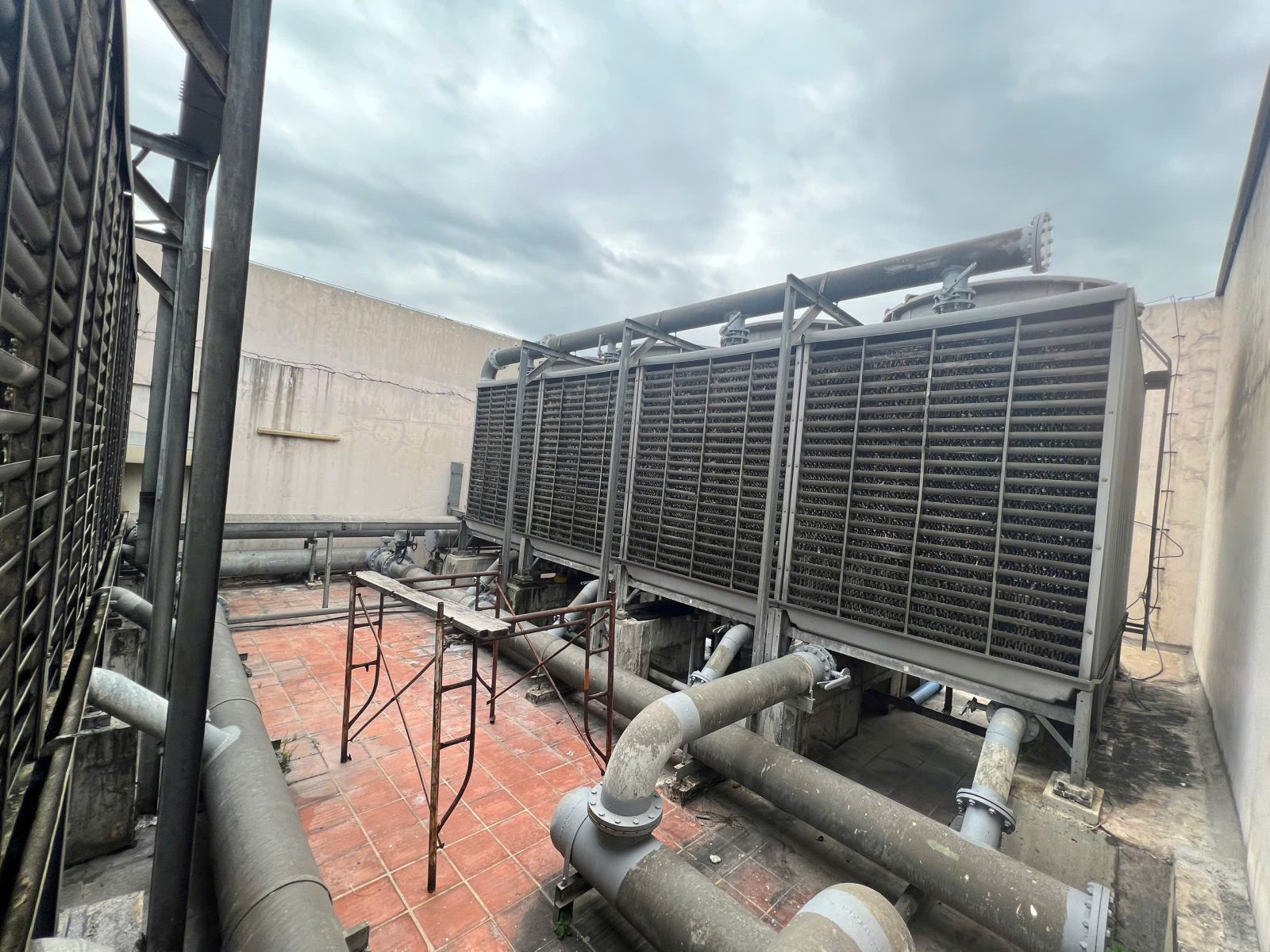 Thanh Lý Hệ Thống Máy Lạnh Công Nghiệp: Cụm thiết bị giải nhiệt lớn với mặt lấy gió dạng nan, quạt phía trên và đường ống mặt bích.